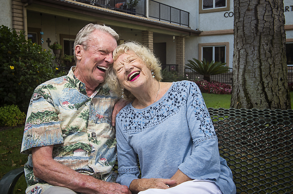 elderly couple laughing and sitting on an outdoor bench