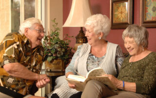 three senior residents sitting indoors reading and chatting