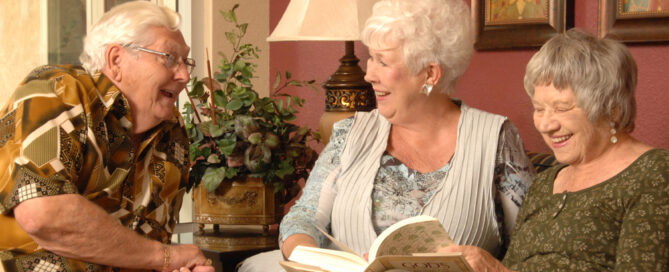 three senior residents sitting indoors reading and chatting