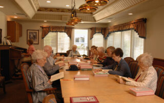 group of senior residents sitting at a long indoor table reading the bible