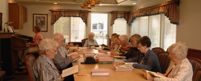 group of senior residents sitting at a long indoor table reading the bible