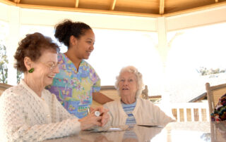 nurse speaking to two resident women sitting at an outdoor table in the shade