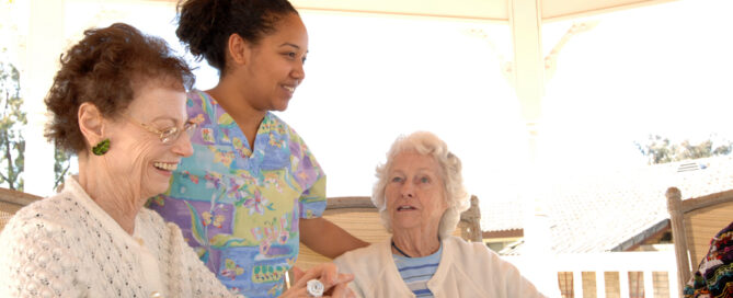 nurse speaking to two resident women sitting at an outdoor table in the shade