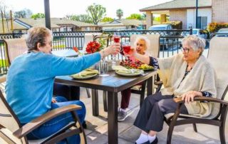 four senior women sitting outside at a patio table holding their glasses up to cheers