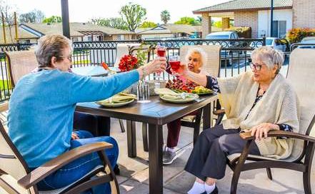 four senior women sitting outside at a patio table holding their glasses up to cheers