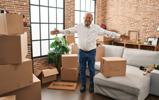 senior man smiling and holding his arms out surrounded by moving boxes