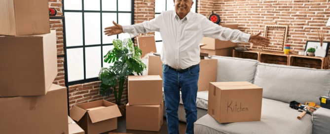 senior man smiling and holding his arms out surrounded by moving boxes