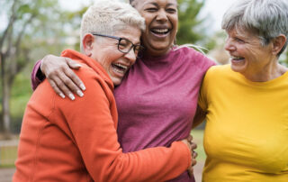 Three senior women in bright clothing group hugging