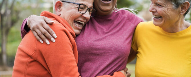 Three senior women in bright clothing group hugging