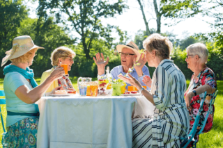 senior friends dining at a table outdoors on a sunny day