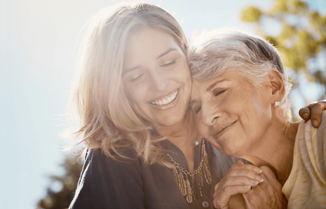 daughter hugging elderly mother outdoors on a sunny day