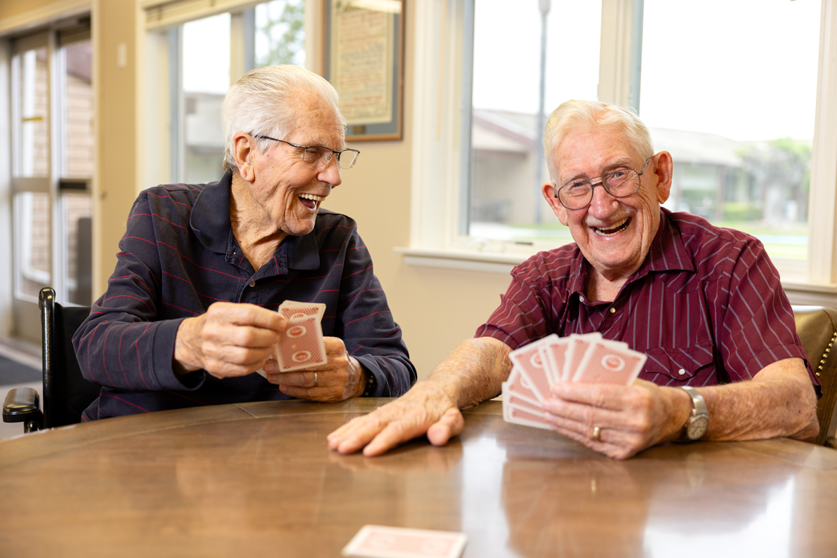 two senior males playing cards at a table indoors