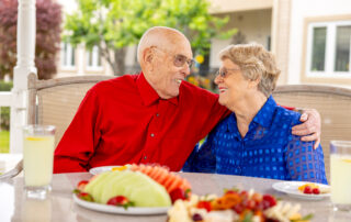 elderly male resident hugging elderly female resident at a table outdoors