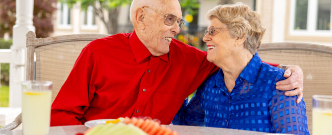 elderly male resident hugging elderly female resident at a table outdoors