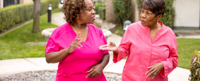 female nurse and female senior resident walking and talking outdoors