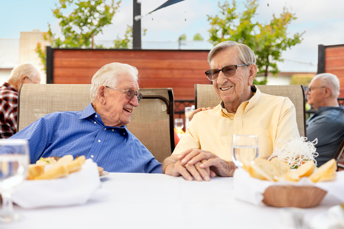 two senior males chatting at an outdoor table